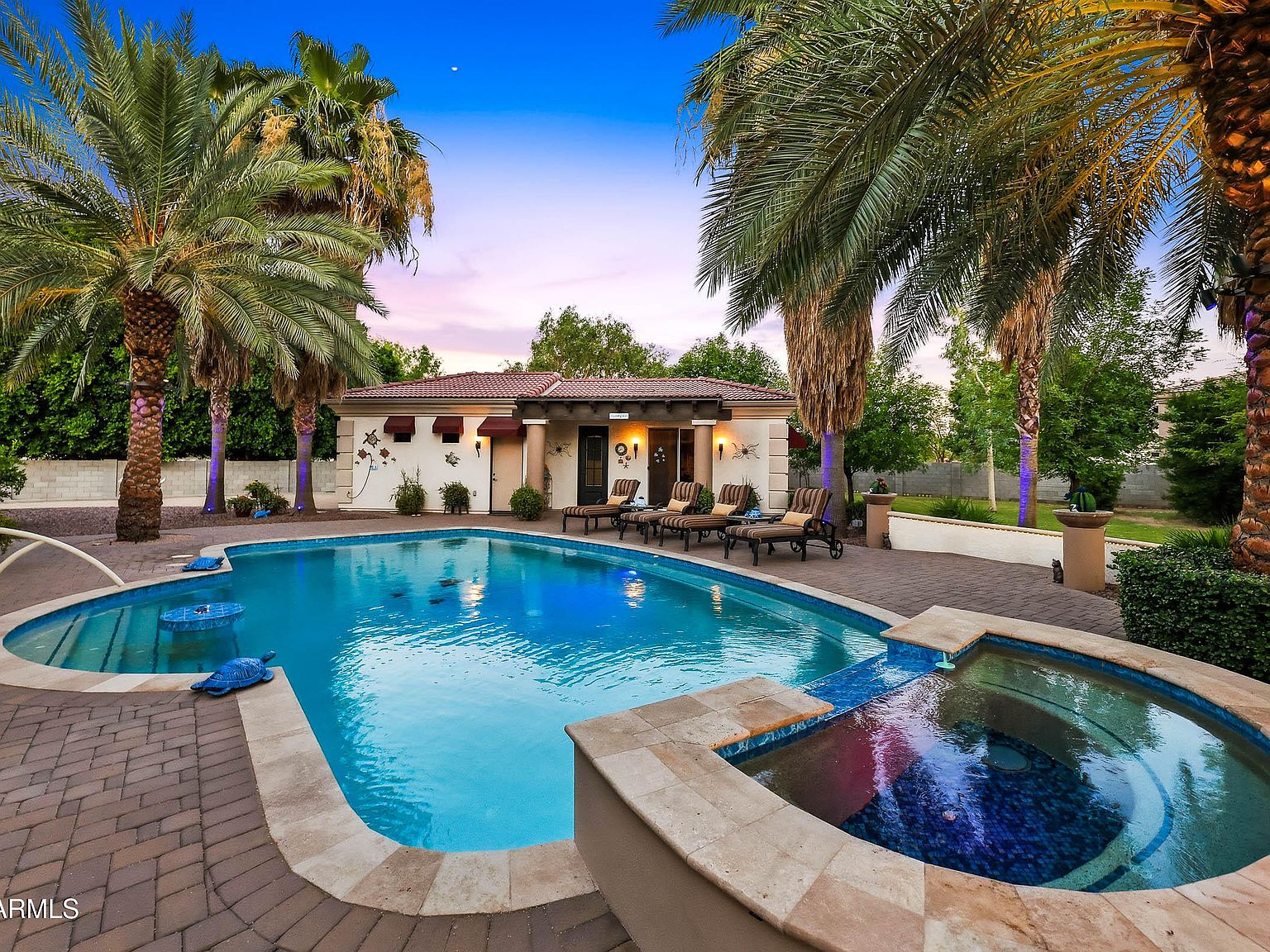 The resort pool and raised spa at twilight, framed by mature date palms, with the lit main house facade and a covered patio behind