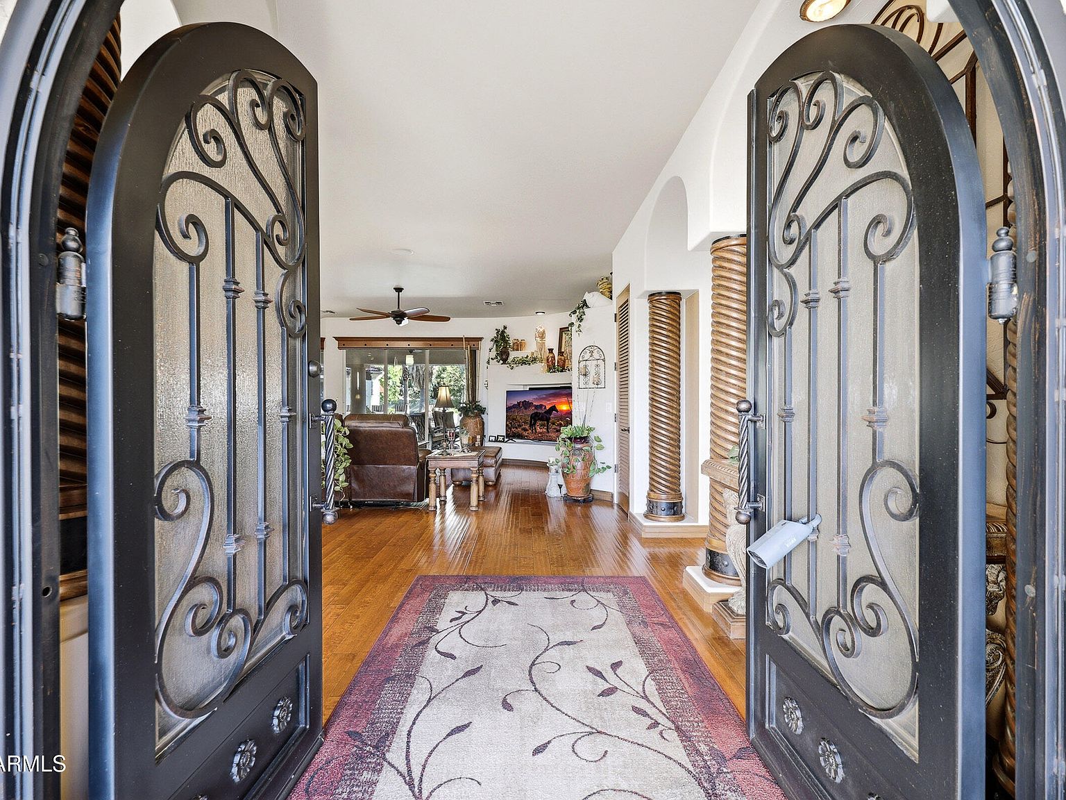 View through the open wrought-iron and glass entry doors into the main living room, with wood flooring, a Western-themed canvas, and a sightline through to the great room