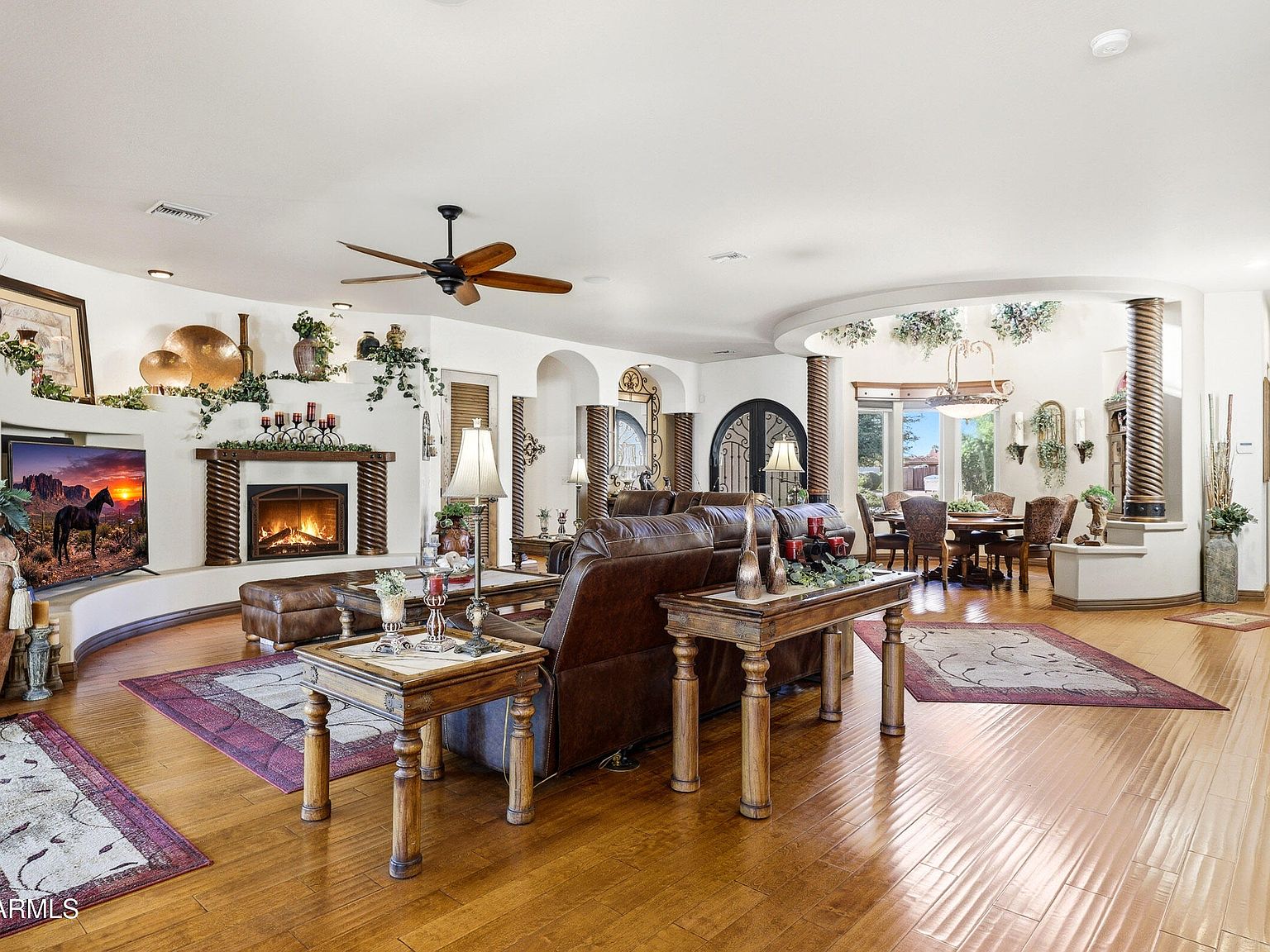 The great room with a gas fireplace, leather seating, a ceiling fan, and a rounded plaster archway leading into the dining area, finished with dark stained alder doors.