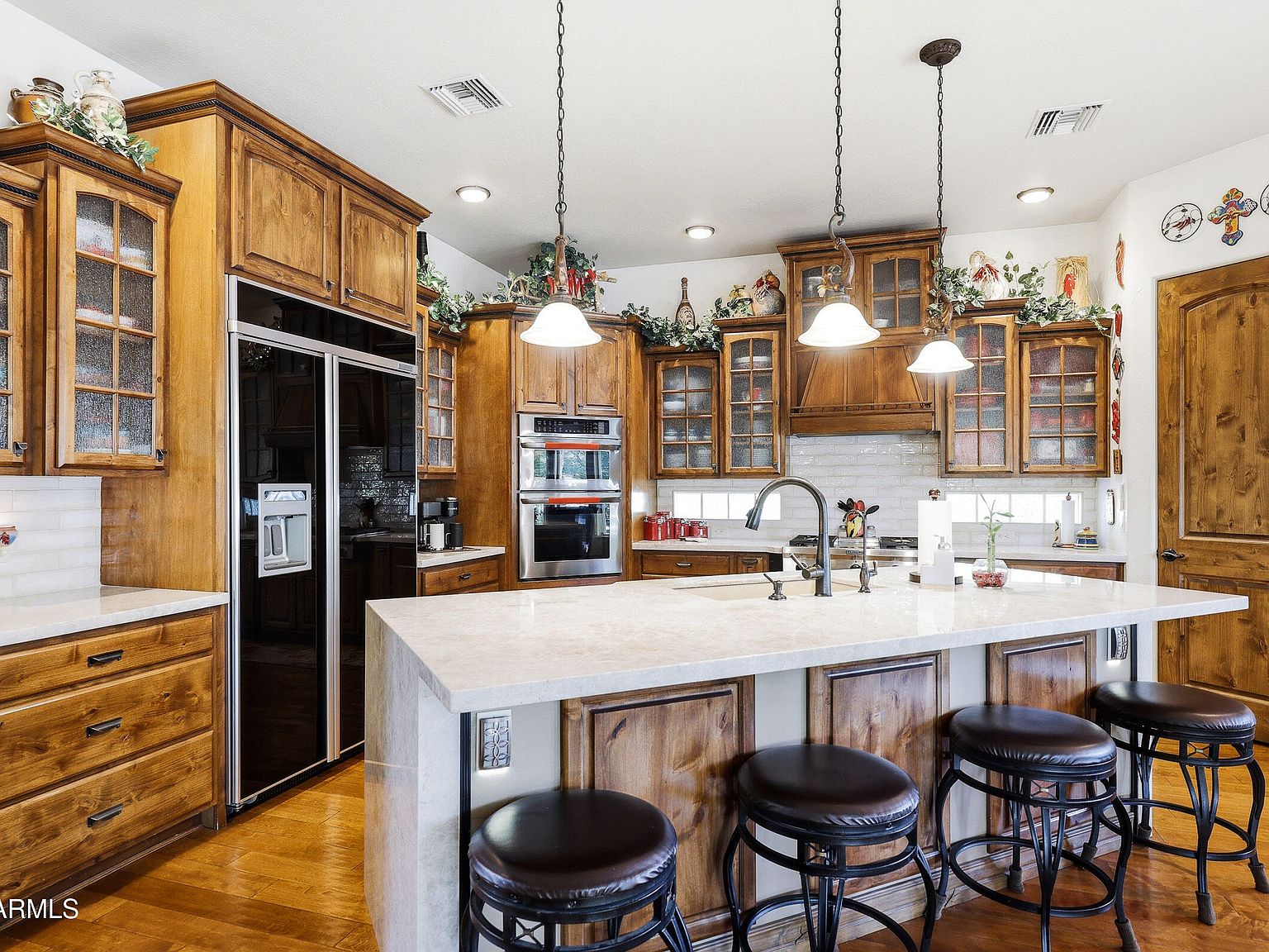 The gourmet kitchen with a large quartz waterfall island, custom alder cabinetry, pendant lighting, and a 48-inch built-in refrigerator