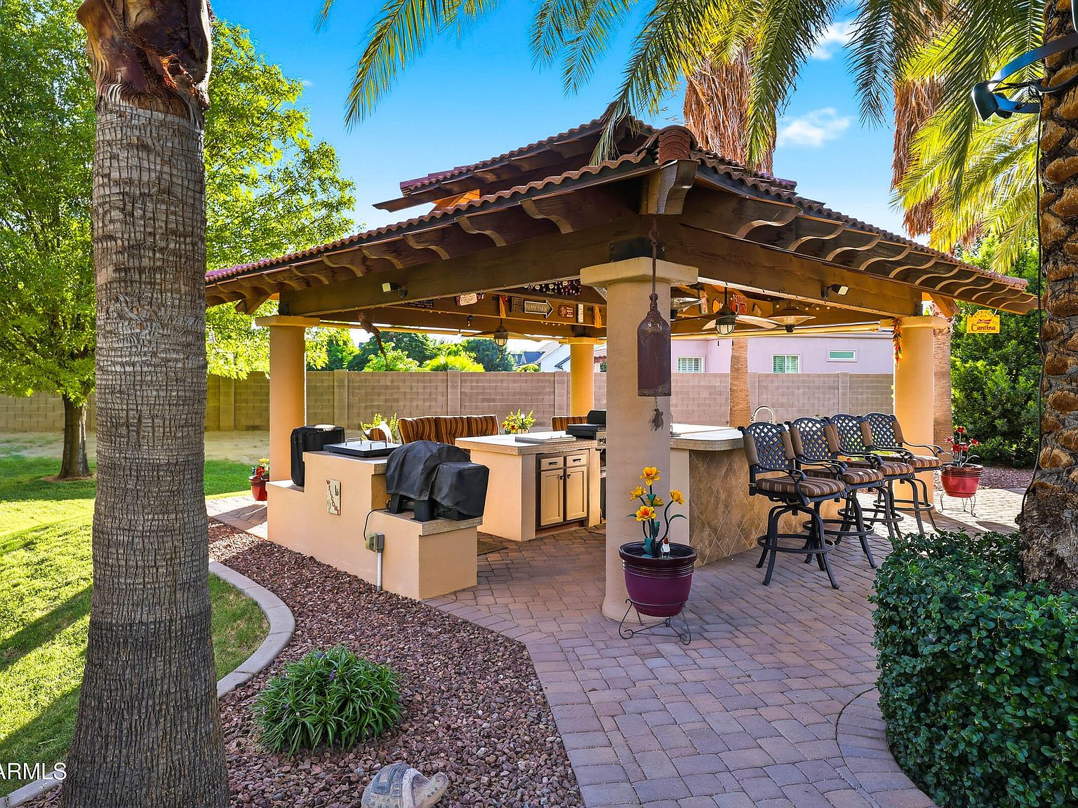 The gazebo bar in daylight, with an exposed timber ceiling, a long bar counter with seating, a stainless grill island, and stools across the bar